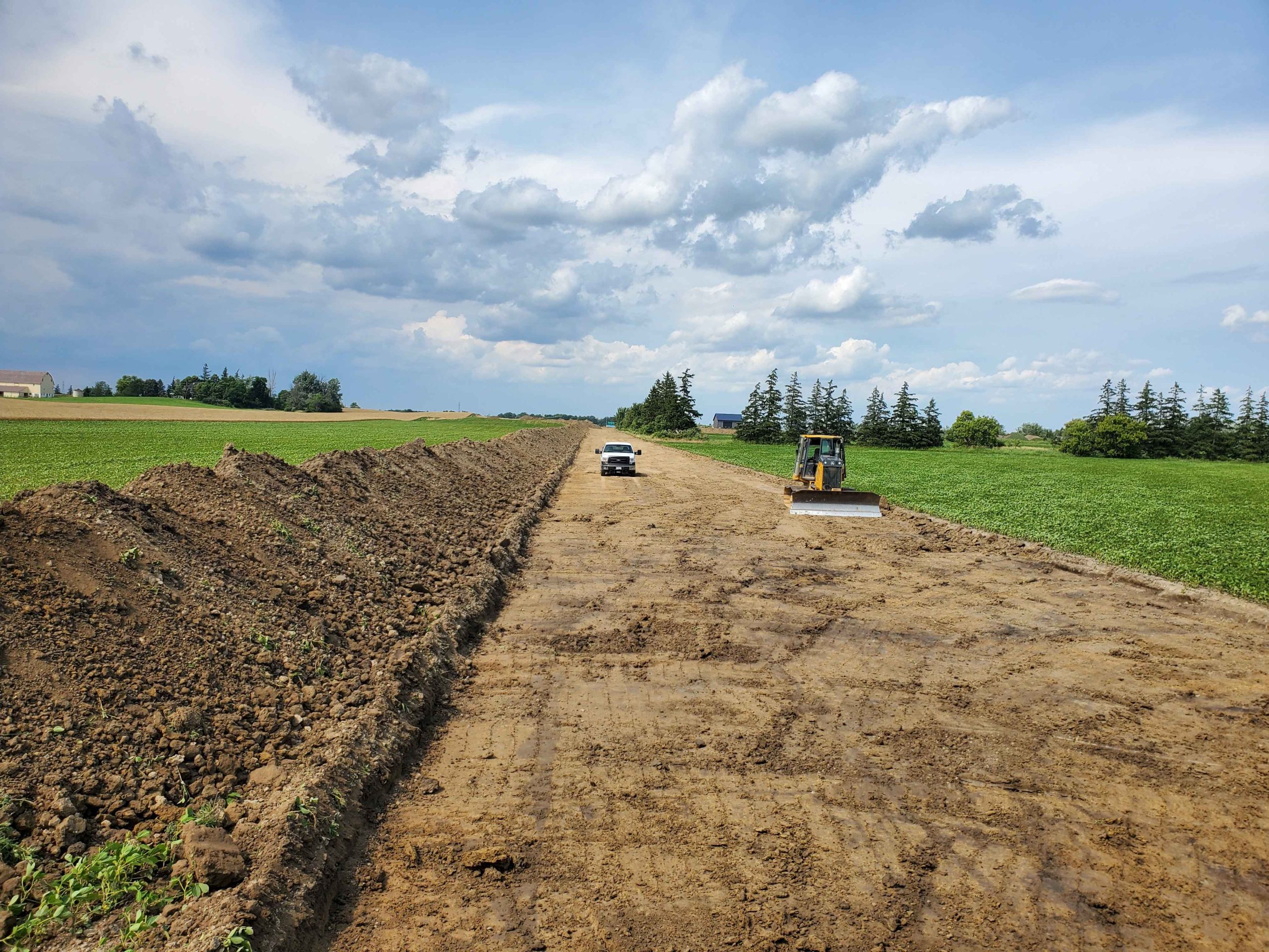 Deere 550K LGP dozer working on a straight road construction project in Haldimand, with a pickup truck providing scale