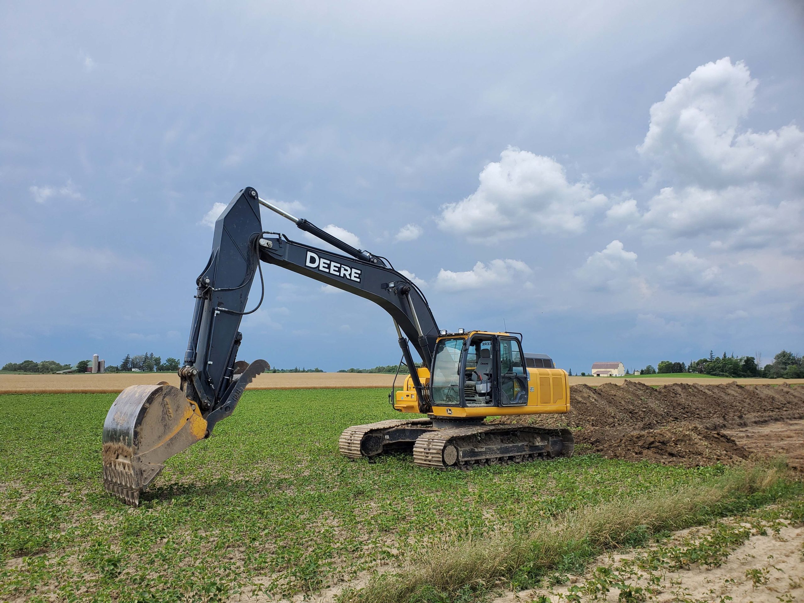 Deere 250G excavator stripping and removing topsoil for farm road construction in Hamilton